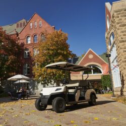 Toro Vista 6-seater golf cart parked near red brick buildings, surrounded by autumn leaves and sunlight, offering spacious seating for passengers