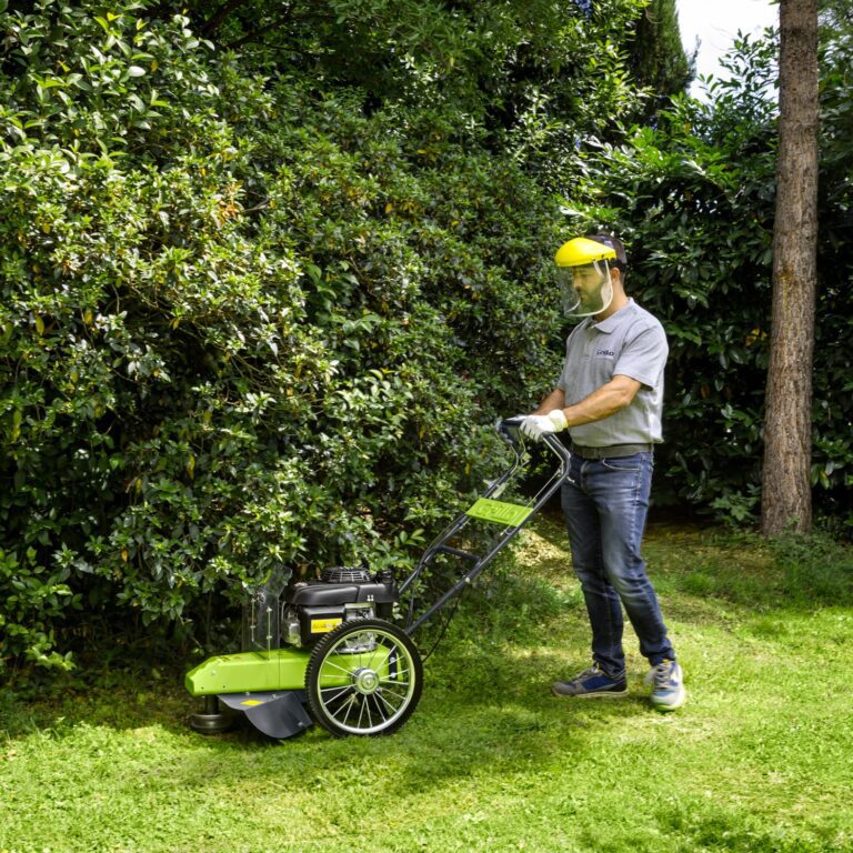 Landscaper man pushing a walk behind tractor over grass underneath shrubs to cut grass