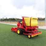 SMG SportChamp SC2D ride-on turf maintenance machine with front and back brushes for effective field cleaning, on artificial turf.