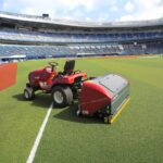 SMG TurfKing TK1502 turf cleaner attached to a red tractor maintaining artificial turf at a large football stadium.