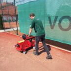 Operator using SMG TurfSoft TS3 artificial grass cleaning machine, working efficiently on a sports field with a red surface.