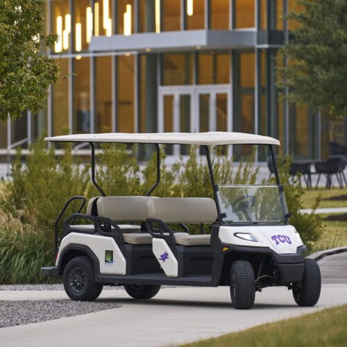 Front-side view of the Toro Vista 4 golf cart with decals, beige seats, and a sleek white exterior, parked in a landscaped area