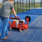 SMG TurfSoft TS3 artificial turf cleaner being operated on blue turf, effectively sweeping debris with its large rotating brush.